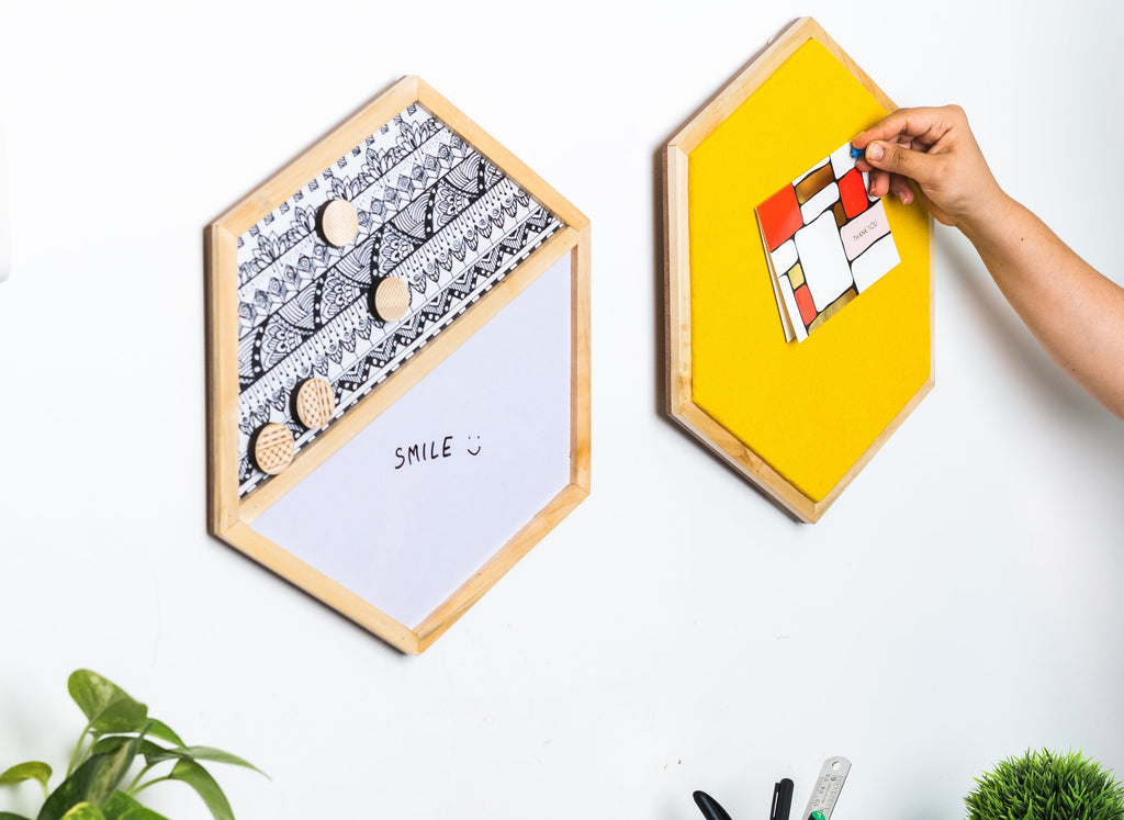 Hexagonal wooden boards with magnetic strips on a wall, one being used to attach a colorful magnet.